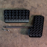 Two black metal foot pedals with a tool on a textured surface